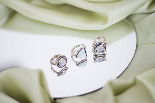 Three silver rings on a mirror - two moonstone and one aurora opal