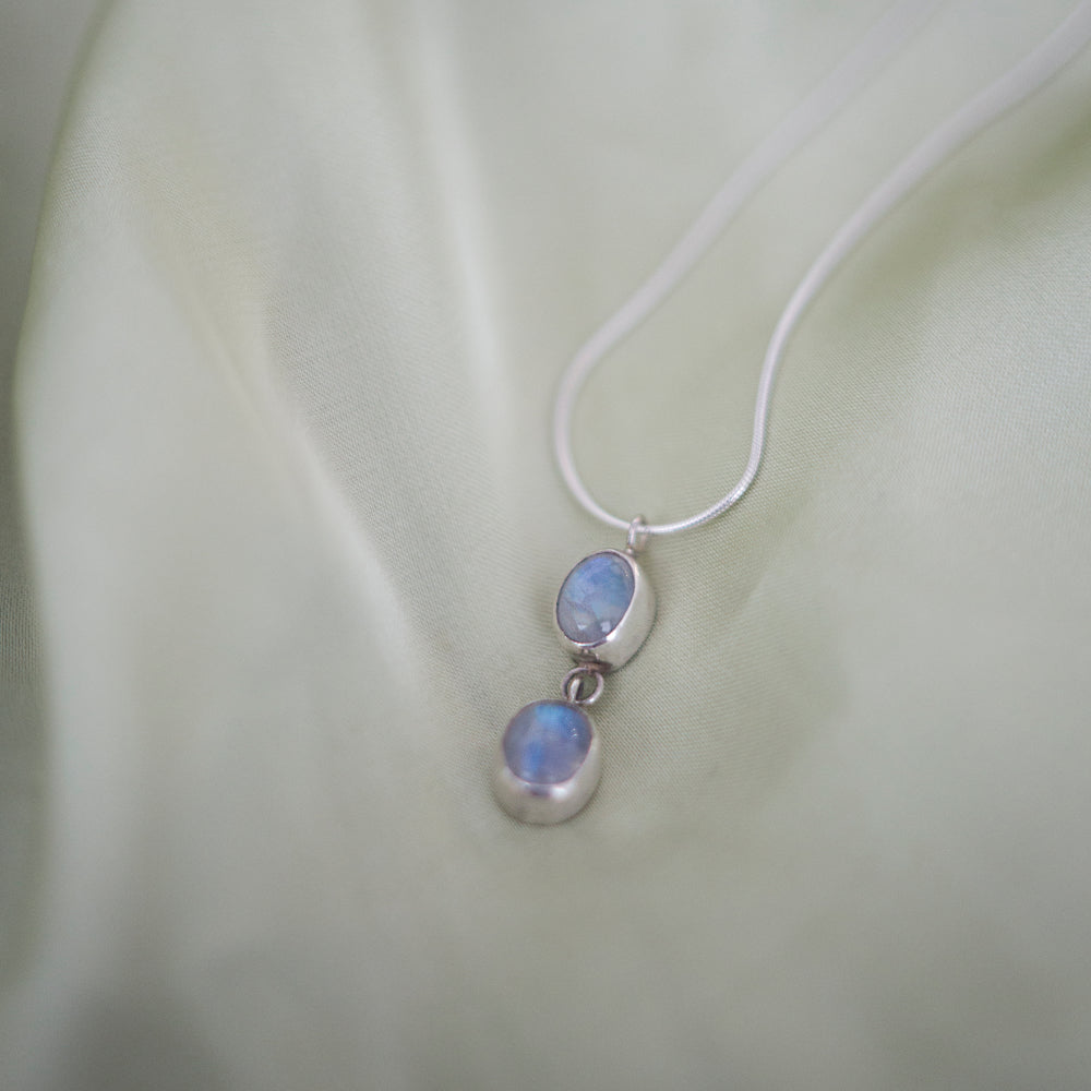 Silver necklace with two moonstone pendants on a light fabric background