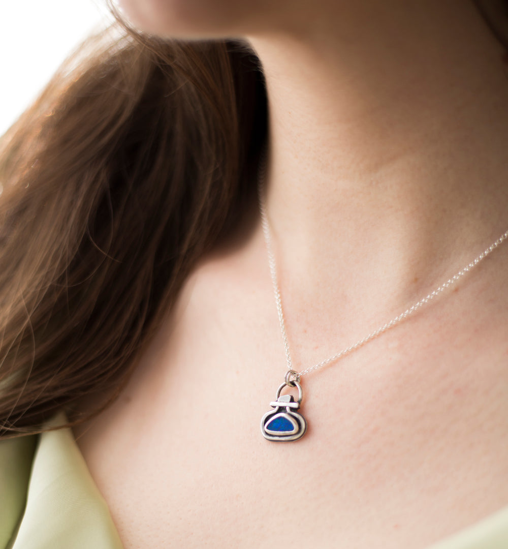 A close-up of a person wearing a delicate silver chain necklace with a small pendant featuring a blue opal doublet.