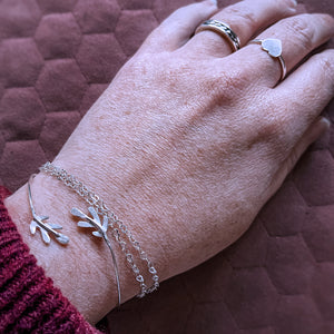 hand on pink cushioned background showing the beau ring, vida ring, meleth cuff and hearth chain bracelet being worn