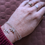 hand on pink cushioned background showing the beau ring, vida ring, meleth cuff and hearth chain bracelet being worn